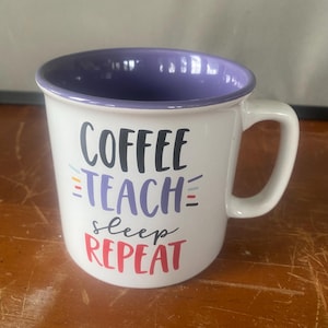 May include: A white ceramic mug with a purple interior and handle. The front features the text COFFEE in black, TEACH in purple, sleep in black, and REPEAT in red, accented by small colorful horizontal lines on the left and right sides.