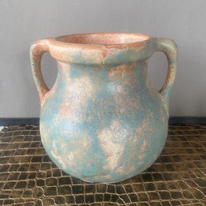 May include: A ceramic vase with two handles, featuring a rounded body and a wide opening. The vase has a mottled blue and brown finish, with a textured appearance. The handles are curved and extend from the rim. The vase is likely for decorative purposes.
