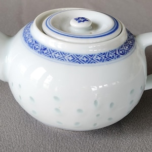May include: A white teapot with a blue and white patterned design. The teapot has a lid and a handle. The teapot is made of ceramic and has a small spout.