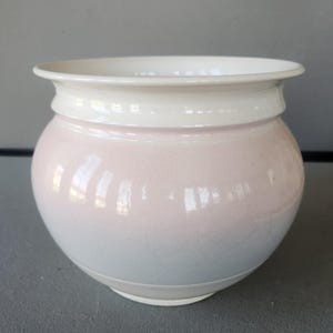 May include: A ceramic planter with a rounded body and a wide, slightly flared rim. The planter features a gradient of colors, transitioning from a soft pink at the top to a pale blue at the base, with a white rim.