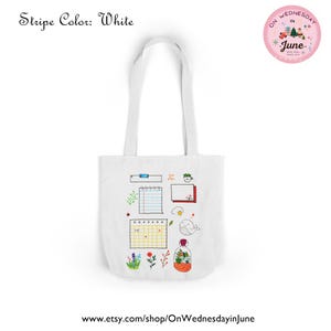 Puede incluir: Bolso tote blanco con ilustraciones dibujadas a mano, incluyendo un calendario, una ballena y flores. El bolso tiene asas largas y el texto "Stripe Color: White" es visible.