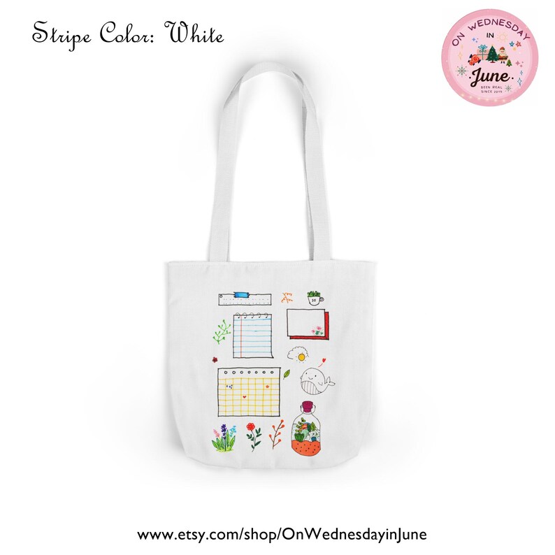 Puede incluir: Bolso tote blanco con ilustraciones dibujadas a mano, incluyendo un calendario, una ballena y flores. El bolso tiene asas largas y el texto "Stripe Color: White" es visible.