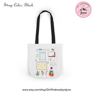 Puede incluir: Bolso tote blanco con correas negras. Presenta ilustraciones de garabatos coloridos de un calendario, ballena, flores y un terrario. Una pegatina circular rosa dice "On Wednesday in June".