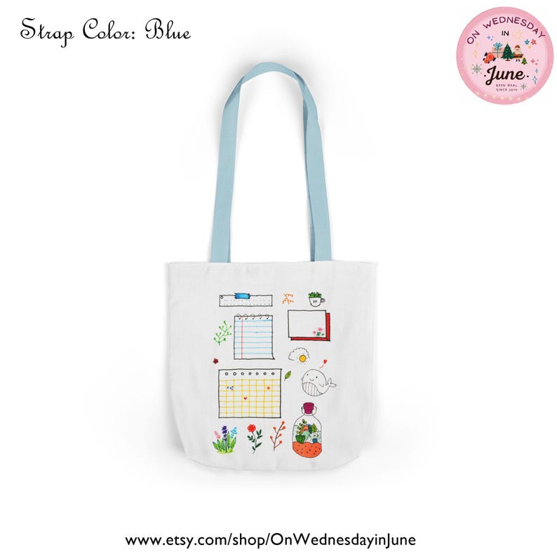 Puede incluir: Bolso tote blanco con correas azul claro. La bolsa presenta un dise&ntilde;o caprichoso con elementos dibujados a mano que incluyen un calendario, un cuaderno, una ballena y flores. El texto "Strap Color: Blue" est&aacute; en la parte superior izquierda.