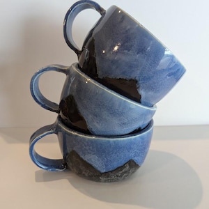 May include: Three blue ceramic mugs with black mountain designs stacked on top of each other.
