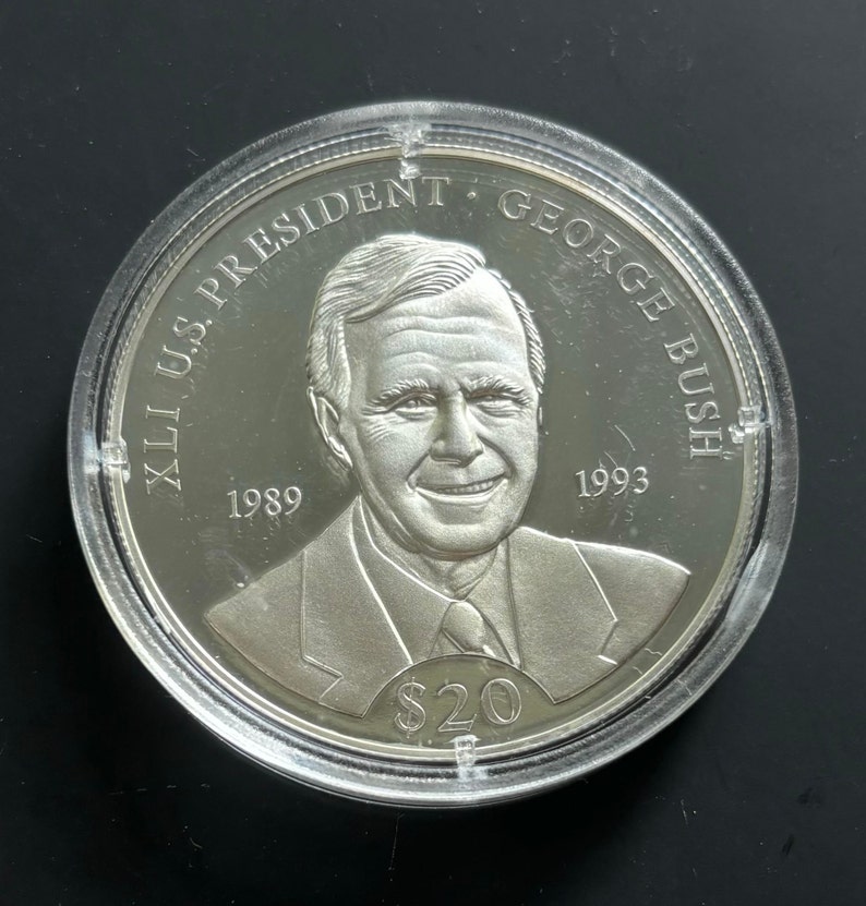 May include: Silver commemorative coin featuring a portrait of George H.W. Bush, the 41st U.S. President, with the text "XLI U.S. PRESIDENT GEORGE BUSH" and the years "1989" and "1993" around the portrait. The coin also has the text "$20" at the bottom.