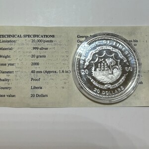 May include: A silver proof coin from Liberia, featuring the country's coat of arms with a ship and palm trees. The coin is dated 2000 and has a face value of 20 Dollars. The coin is displayed in a plastic case with a white card that lists technical specifications.