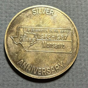 May include: A silver commemorative coin celebrating the 25th anniversary of Monsanto in 1987. The coin features a map of the state of Missouri with the text "A Celebration on the Bayou 1962-1987 Monsanto 25 Years Anniversary".