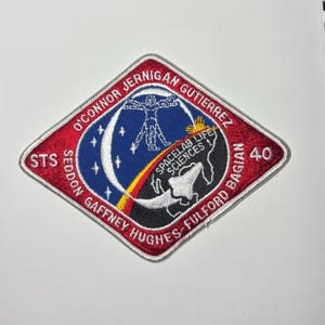 May include: A diamond-shaped embroidered patch with a red border featuring the text O'CONNOR JERNIGAN GUTIERREZ SEDDON GAFFNEY HUGHES-FULFORD BAGIAN STS 40 SPACELAB LIFE SCIENCES 1. The center depicts a white Vitruvian Man, a crescent moon, and a space shuttle.