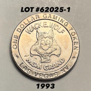 May include: A silver-colored one-dollar gaming token from the MGM Grand in Las Vegas, Nevada. The token features a cartoon wolf character and the text "WACKE. WOLF" and "1993". The text "ONE DOLLAR GAMING TOKEN" is also visible.