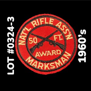 May include: A vintage red and black embroidered patch with the text "NAT'L RIFLE ASSN" and "MARKSMAN AWARD". The patch features crossed rifles and the text "50 FT". The text "LOT #0324-3" and "1960's" are also visible.