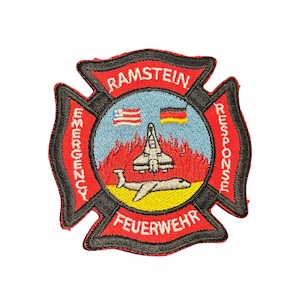 May include: Embroidered patch featuring the words "RAMSTEIN EMERGENCY RESPONSE FEUERWEHR" in a Maltese cross design. The patch includes a central circular emblem with a jet, flames, and flags of Liberia and Germany. The patch is red, black, yellow, blue, and white.