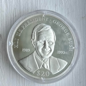 May include: A silver commemorative coin featuring a portrait of George H.W. Bush, the 41st U.S. President. The coin reads "41st U.S. President George Bush" and "1989 - 1993". The coin also has a denomination of $20.
