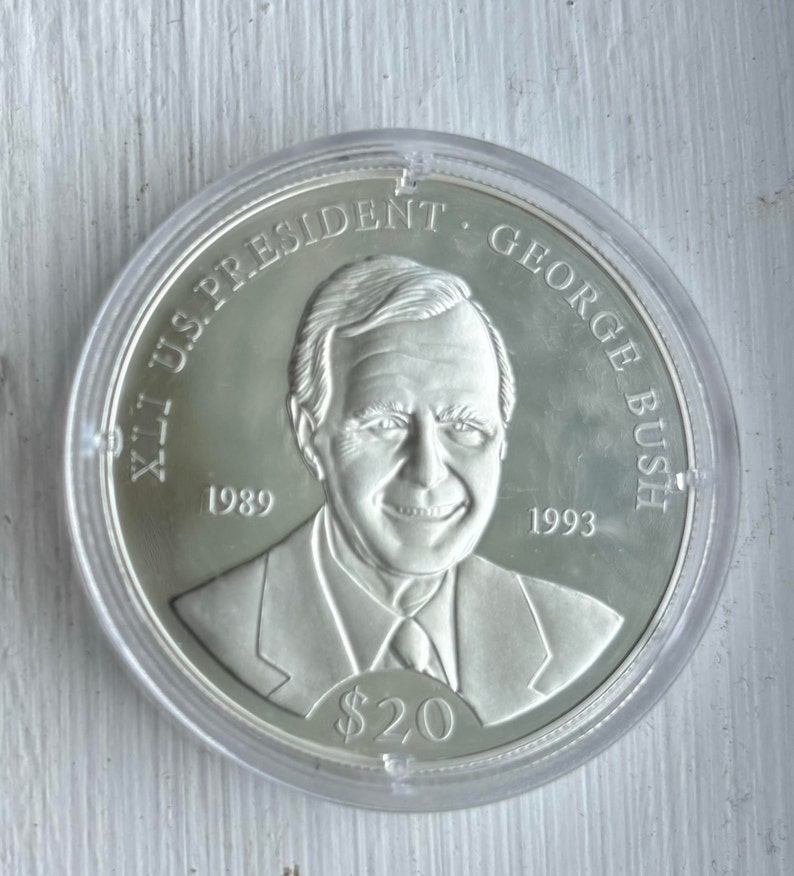 May include: A silver commemorative coin featuring a portrait of George H.W. Bush, the 41st U.S. President. The coin reads "41st U.S. President George Bush" and "1989 - 1993". The coin also has a denomination of $20.