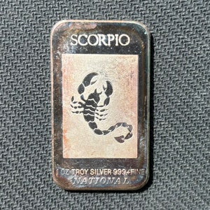 May include: A silver bar with a scorpion design and the text "SCORPIO" and "1 oz TROY SILVER 999.9 FINE NATIONAL".