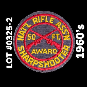 May include: A vintage patch from the 1960s, featuring the text "NAT'L RIFLE ASSN" and "SHARPSHOOTER AWARD". The patch has a circular design with crossed rifles in red, yellow, and gray. The text "50 FT" is also visible.