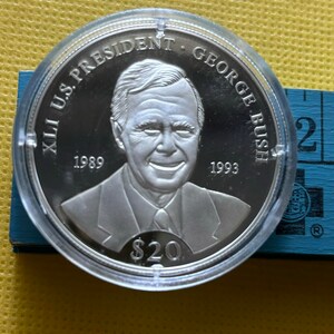 May include: A silver commemorative coin featuring a portrait of George H.W. Bush, the 41st U.S. President. The coin reads "XLI U.S. PRESIDENT GEORGE BUSH" and includes the years "1989" and "1993". The coin also features the denomination "$20".
