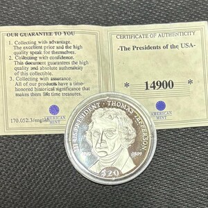 May include: A silver coin depicting Thomas Jefferson, with the text "US PRESIDENT THOMAS JEFFERSON" and "1809". Includes a certificate of authenticity and a guarantee document from the American Mint.