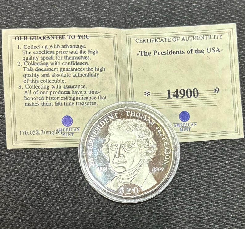 May include: A silver coin depicting Thomas Jefferson, with the text "US PRESIDENT THOMAS JEFFERSON" and "1809". Includes a certificate of authenticity and a guarantee document from the American Mint.