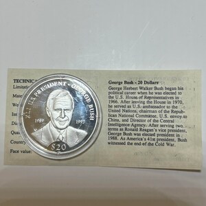 May include: A silver commemorative coin featuring a portrait of George H.W. Bush, the 41st president of the United States. The coin is inscribed with "41st U.S. President George Bush" and the years "1989" and "1993". The coin has a face value of $20.