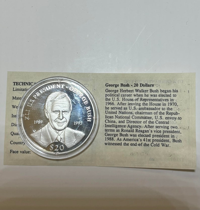 May include: A silver commemorative coin featuring a portrait of George H.W. Bush, the 41st president of the United States. The coin is inscribed with "41st U.S. President George Bush" and the years "1989" and "1993". The coin has a face value of $20.