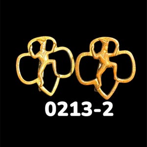 May include: Two gold-colored Girl Scout pins. Each pin features a stylized figure within a trefoil shape. The pins are set against a black background. The number "0213-2" is printed in white below the pins.