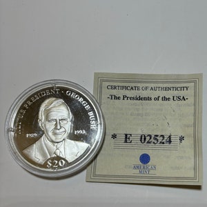 May include: A silver coin with a portrait of George H.W. Bush, the 41st President of the United States. The coin is inscribed with "41st U.S. President George Bush" and the years "1989" and "1993". The coin is also inscribed with "$20". The coin is accompanied by a certificate of authenticity from the American Mint.
