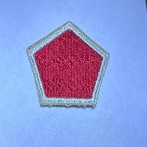 May include: A pentagonal embroidered patch featuring a solid red center surrounded by a thick, light-colored border. The stitching is dense and uniform, creating a textured surface across the entire shape of the patch, which has five distinct sides.