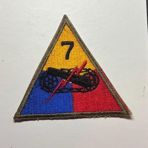 May include: A triangular embroidered patch featuring a yellow top section with the black number 7, a blue bottom left section, and a red bottom right section. A black tank tread graphic is centered with a red lightning bolt overlaying it.
