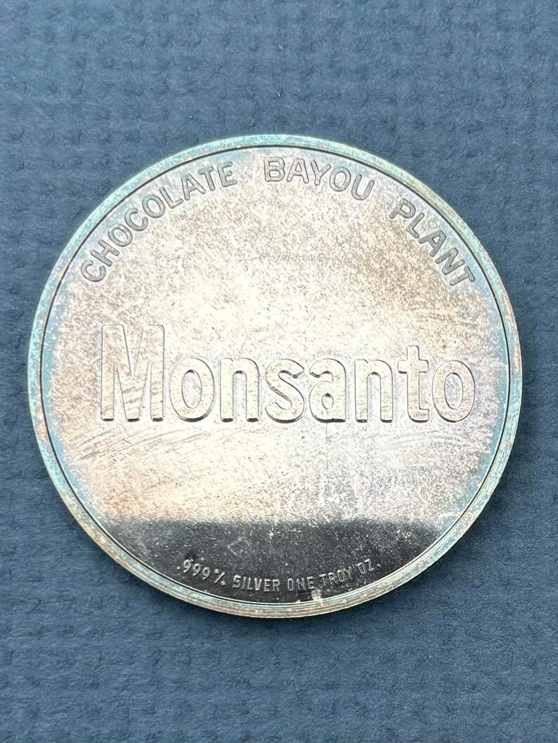 May include: A silver coin with the words "Chocolate Bayou Plant Monsanto" and "999 1/2 Silver One Troy Oz." inscribed on it.