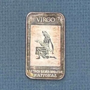May include: A silver bar with the zodiac sign Virgo and the text "1 oz Troy Silver 999+ Fine National".