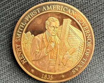 May include: A gold-coloured coin featuring a portrait of Henry Smith, the first American governor of Texas. The coin is inscribed with "Henry Smith First American Governor of Texas" and "1835".