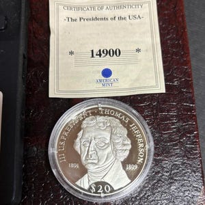 May include: A silver coin featuring Thomas Jefferson, with the text "III U.S. PRESIDENT THOMAS JEFFERSON" and the years 1801 and 1809. The coin is in a clear plastic case, with a certificate of authenticity from the American Mint.