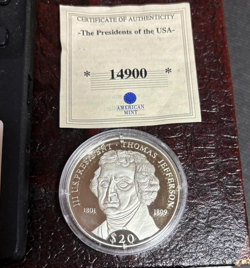 May include: A silver coin featuring Thomas Jefferson, with the text "III U.S. PRESIDENT THOMAS JEFFERSON" and the years 1801 and 1809. The coin is in a clear plastic case, with a certificate of authenticity from the American Mint.