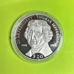 May include: A silver coin depicting Thomas Jefferson, with the inscription "III U.S. PRESIDENT THOMAS JEFFERSON" and the years 1801 and 1809. The coin is marked with "$20" and is in a clear plastic case.