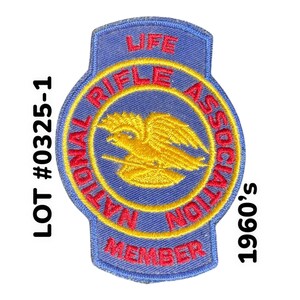 May include: A blue and yellow embroidered patch with the text "National Rifle Association Life Member" and a yellow eagle design. The text "LOT # 0325-1 1960's" is printed on the right side of the image.