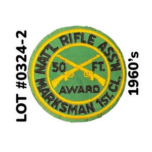 May include: A circular green and yellow embroidered patch with text and crossed rifles. The patch reads "NAT'L RIFLE ASSN" and "MARKSMAN 1ST CL" with "50 FT AWARD" in the center. The text "LOT #0324-2" and "1960's" are also visible.