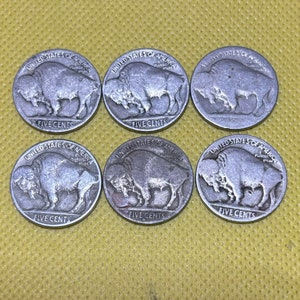 May include: Six silver US five-cent coins featuring the profile of a buffalo with the words "United States of America" and "Five Cents" inscribed on each coin.