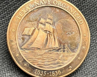 May include: A bronze coin with the text "TEXAS NAVY ORGANIZED" around the edge. The coin features a detailed depiction of a tall ship sailing on the sea, with the years "1835-1836" below. Several stars are also visible.