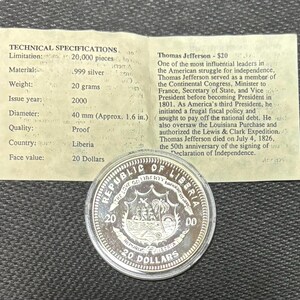 May include: A silver coin from the Republic of Liberia, featuring a sailing ship and palm trees. The coin has a face value of 20 dollars and a diameter of approximately 40 mm. The coin is made of .999 silver and weighs 20 grams.