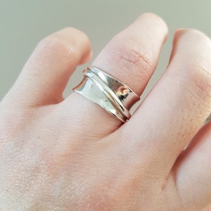 May include: A silver ring with a wide band that wraps around the finger. The band is twisted and has a smooth, polished finish.