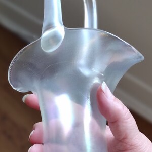 Peut inclure: Un panier en verre transparent irisé avec une poignée. Le panier a un bord festonné et une base texturée.