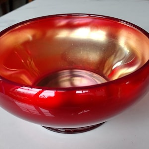 May include: A vibrant red glass bowl with a glossy finish. The interior has a golden hue, creating a striking contrast. The bowl sits on a small, circular base, showcasing a modern design.