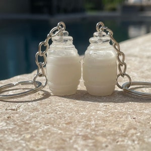 May include: Two white milk jug keychain charms with silver key rings. The charms are made of resin and have a frosted finish.