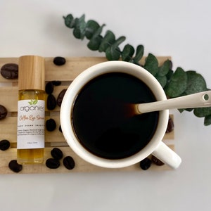 Puede incluir: Una pequeña botella de vidrio marrón con una tapa de madera y una etiqueta blanca que dice "arganier Coffee Eye Serum" en una bandeja de madera con granos de café y una taza de café blanca.