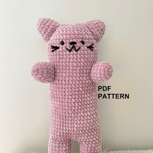 Könnte beinhalten: Ein rosa gehäkeltes Katzenspielzeug mit schwarzen gestickten Augen und einem lächelnden Mund. Das Spielzeug steht auf einem weißen und rosa Teppich. PDF PATTERN.