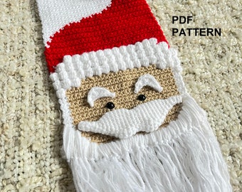 May include: A crocheted wall hanging of Santa Claus's face. The hanging features a white beard, brown face, black eyes, and a white mustache. The top of the hanging is a red and white Santa hat with a white pom-pom.
