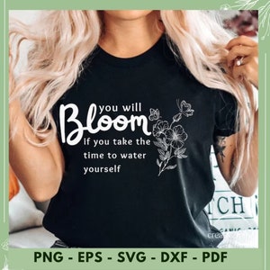 May include: Black t-shirt with white text that reads "you will Bloom if you take the time to water yourself". The text is surrounded by a stylized floral design.