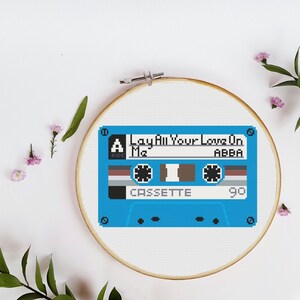 May include: A blue cassette tape cross-stitch pattern with the text "Lay All Your Love On Me" and "ABBA" on it.
