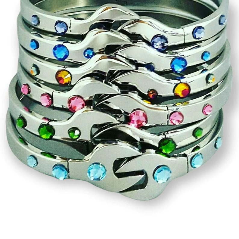 Puede incluir: Una pila de pulseras de plata con un dise&ntilde;o de llave inglesa. Cada pulsera est&aacute; decorada con brillantes de colores.
